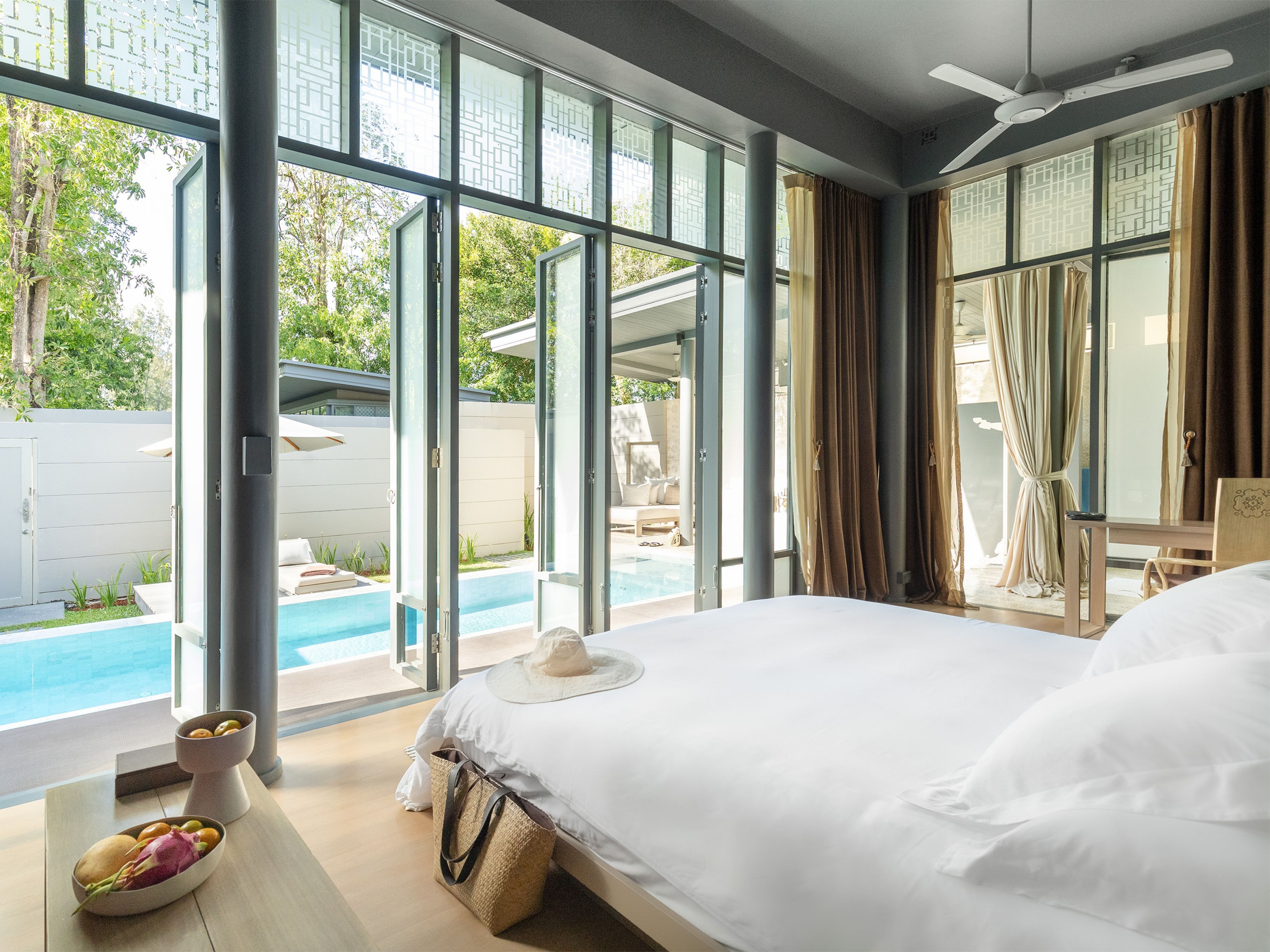 Habitación de hotel con una cama grande, vistas a una piscina y un balcón con mobiliario exterior.