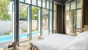 Habitación de hotel con una cama grande, vistas a una piscina y un balcón con mobiliario exterior.