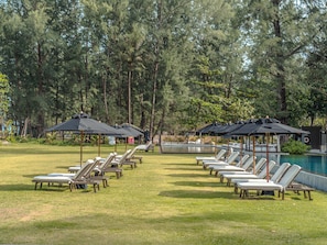 Ein Poolbereich mit Liegestühlen und Sonnenschirmen, umgeben von Bäumen.