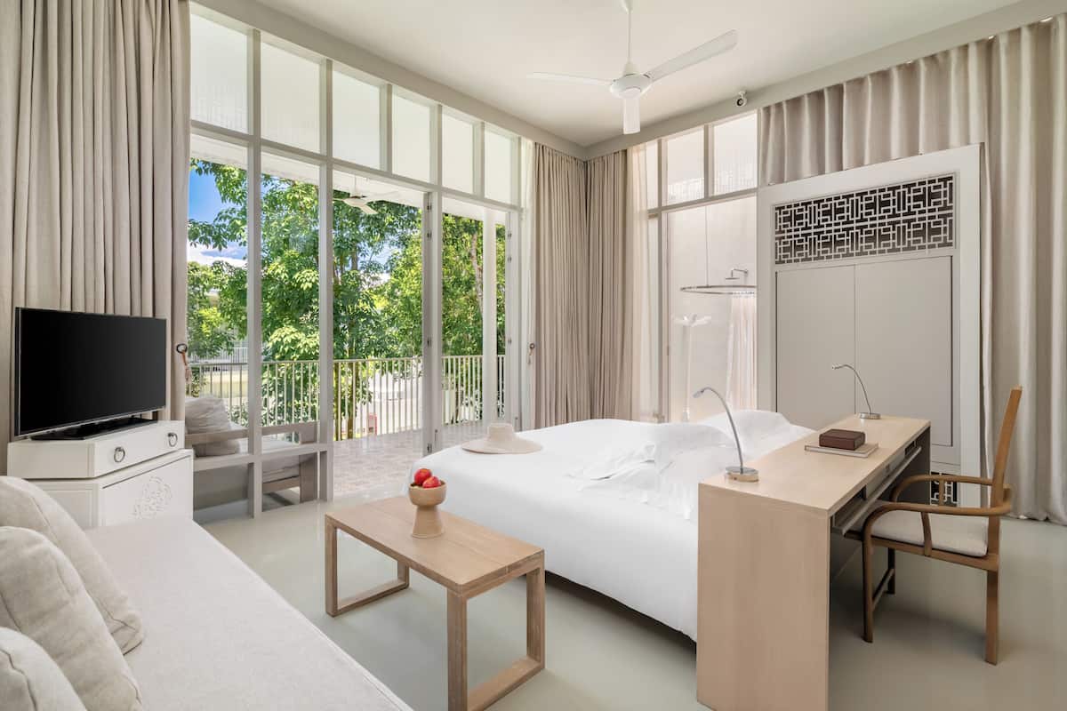 Ein modernes Hotelzimmer mit einem großen Bett, einem Schreibtisch, einem Fernseher und einem Balkon mit Blick auf Grünflächen.