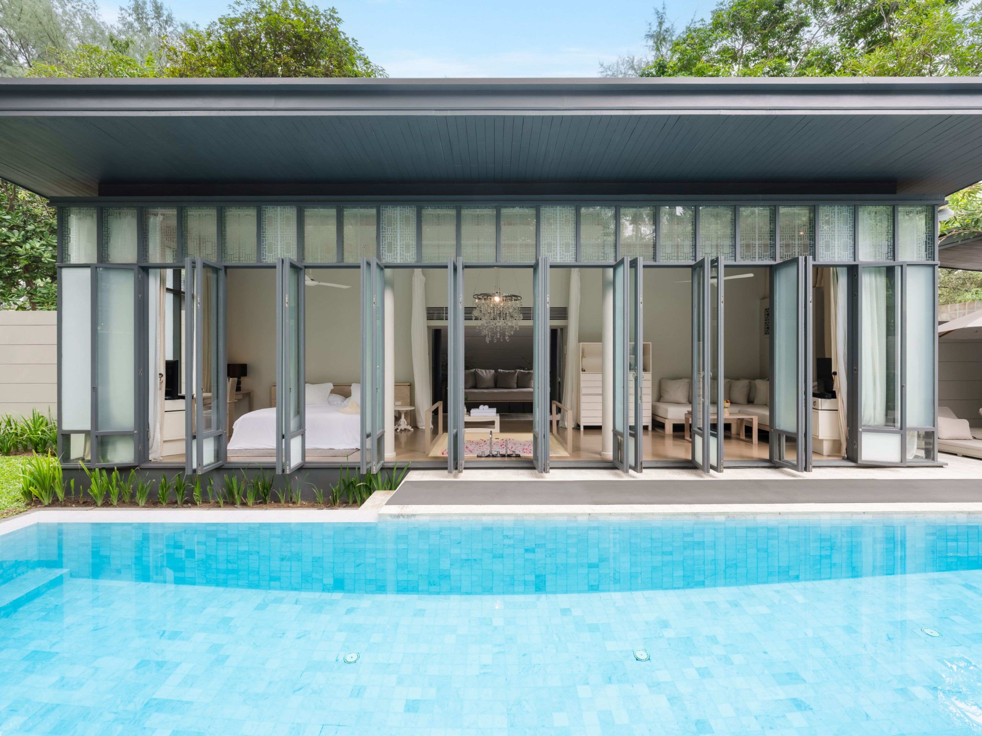 Una casa moderna con piscina, puertas de cristal amplias y un interior espacioso con una araña.