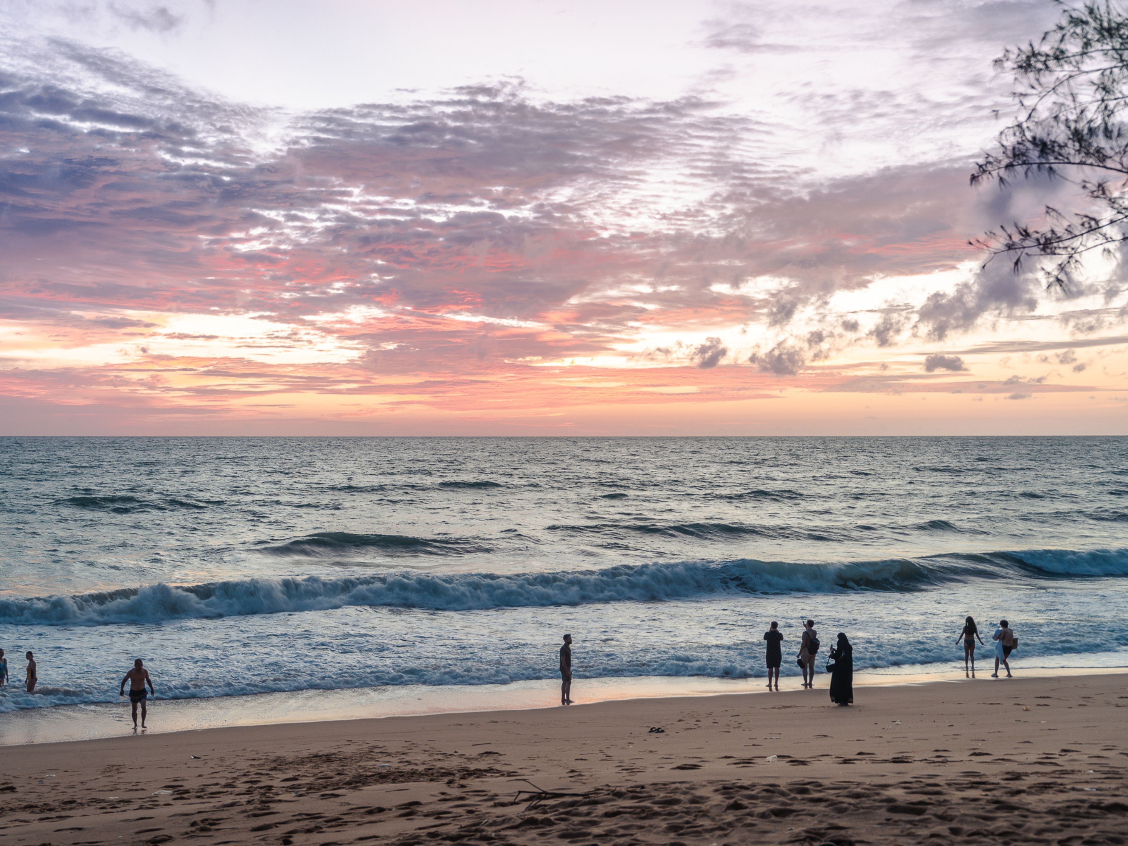 A beach with people walking along the shore and waves crashing onto the sand.
