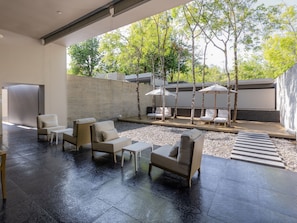 A modern outdoor seating area with lounge chairs and tables, surrounded by a stone wall and trees. - SALA Phuket Mai Khao Beach Resort (Mai Khao)