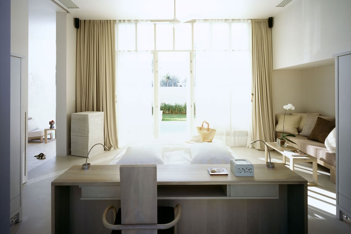 Ein modernes Hotelzimmer mit großem Fenster, Schreibtisch mit Stuhl, einer Couch und einem kleinen Tisch mit Lampe.