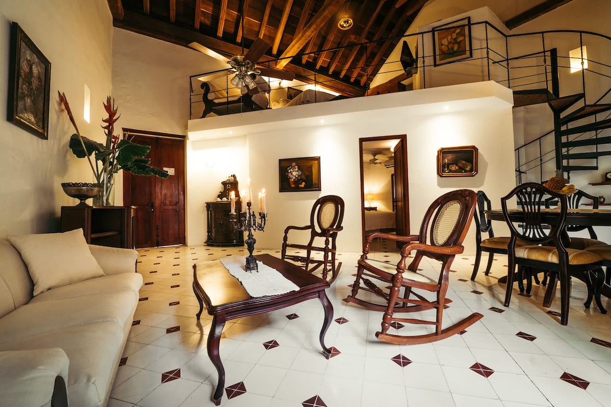 Amplia sala de estar con techos altos, un comedor con mesa y sillas de madera, y una escalera que conduce a un nivel superior.