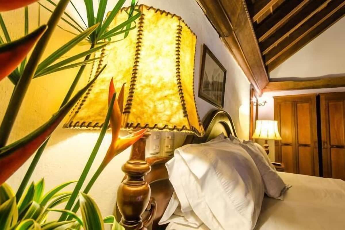 Habitación de hotel con una cama, una lámpara, una puerta de madera y un cuadro en la pared.