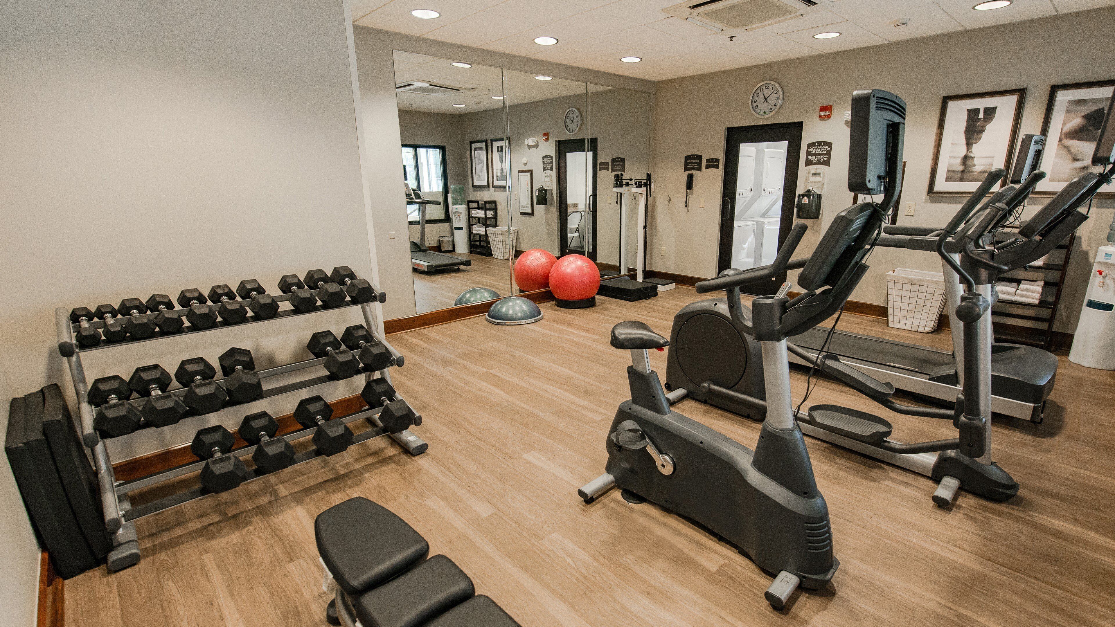 Een fitnessruimte met trainingsapparatuur, waaronder gewichten, een loopband en trainingsballen.