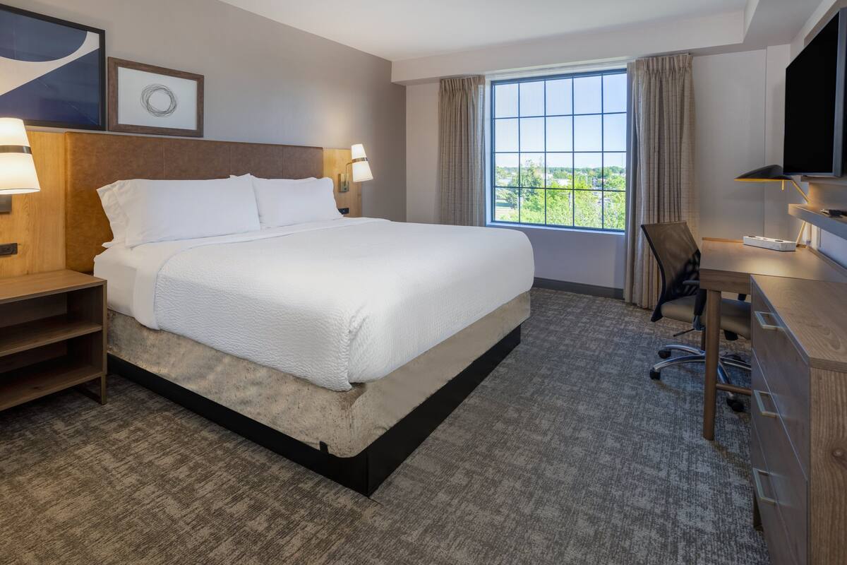 A hotel room with a large bed, a desk, a chair, a television, and a window with a view.