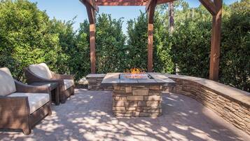Une terrasse extérieure dotée d’une table de feu en pierre, de meubles en osier et d’une structure en forme de pergola.