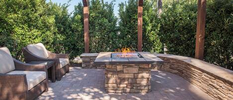 An outdoor patio with a stone fire table, wicker furniture, and a pergola structure.