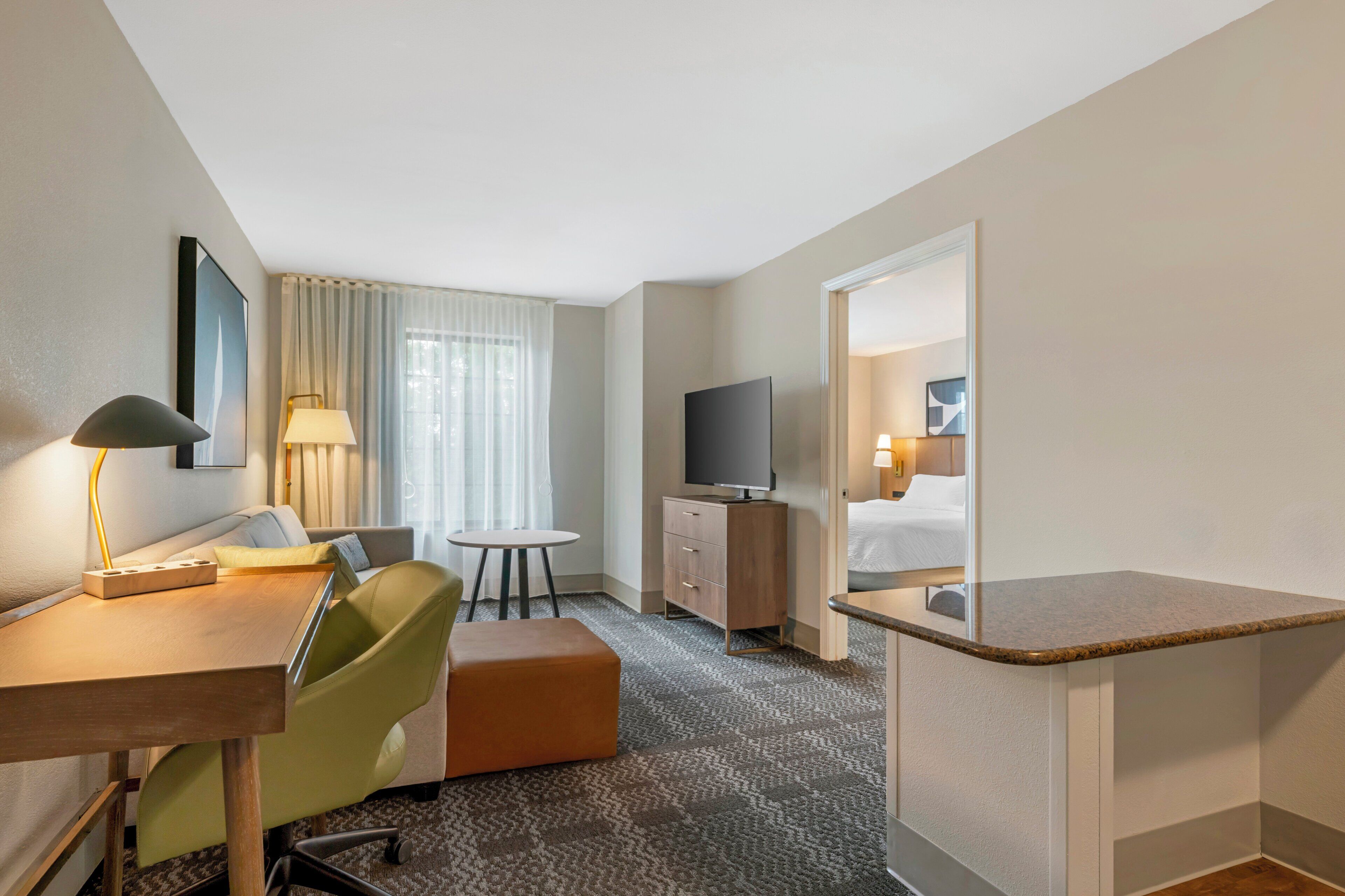 A hotel room with a desk, chair, television, and a bed.