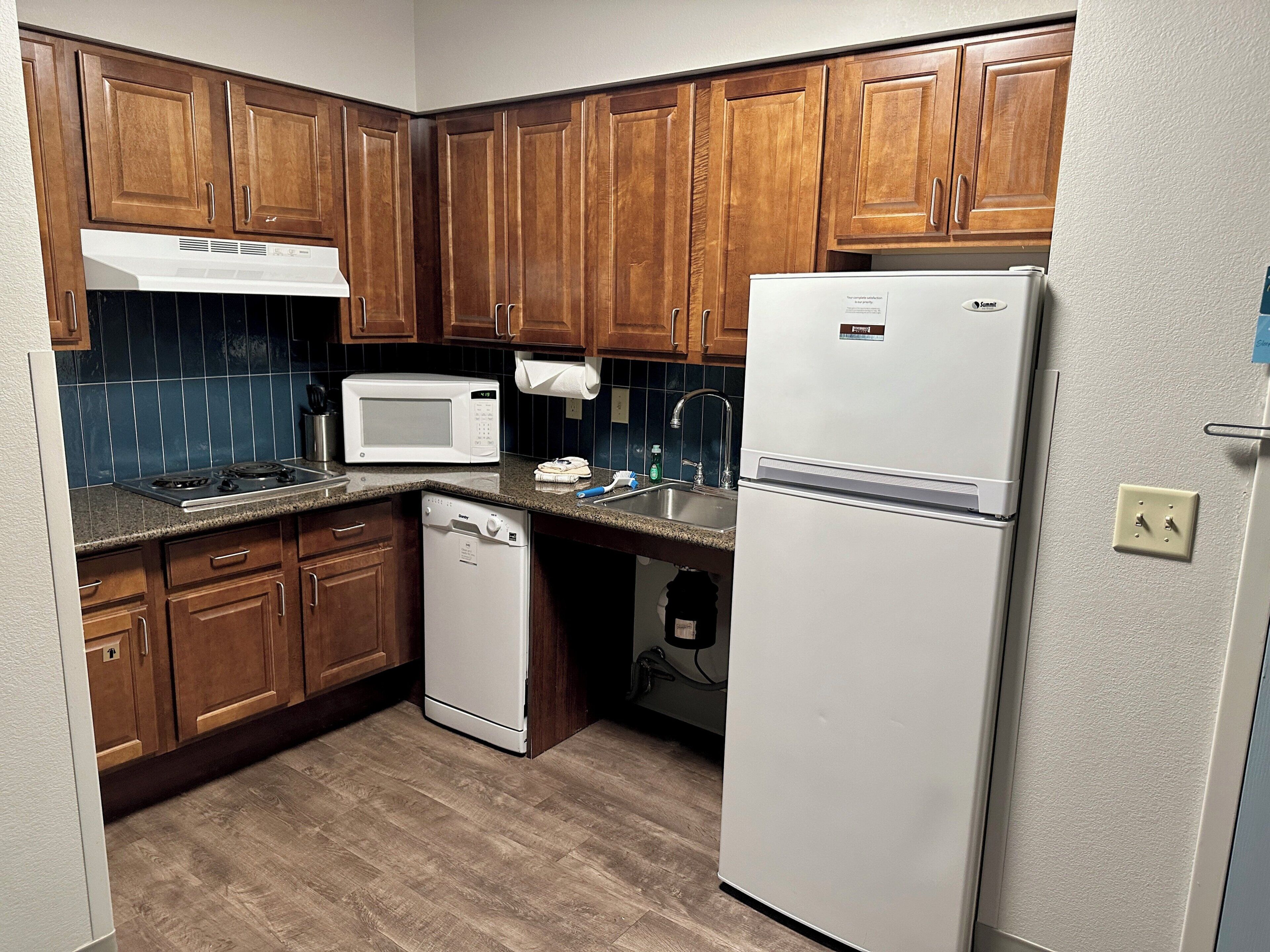 A compact kitchen with wooden cabinets, a microwave, a dishwasher, and a refrigerator.