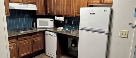 Una cocina compacta con muebles de madera, microondas, lavavajillas y refrigerador.
