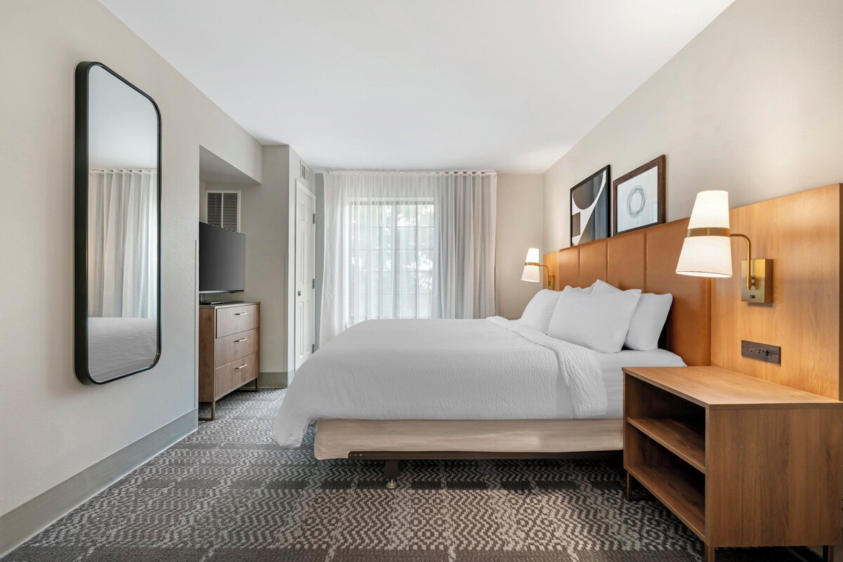 Une chambre d’hôtel avec un grand lit, une table de chevet, une télévision, une armoire et un miroir.