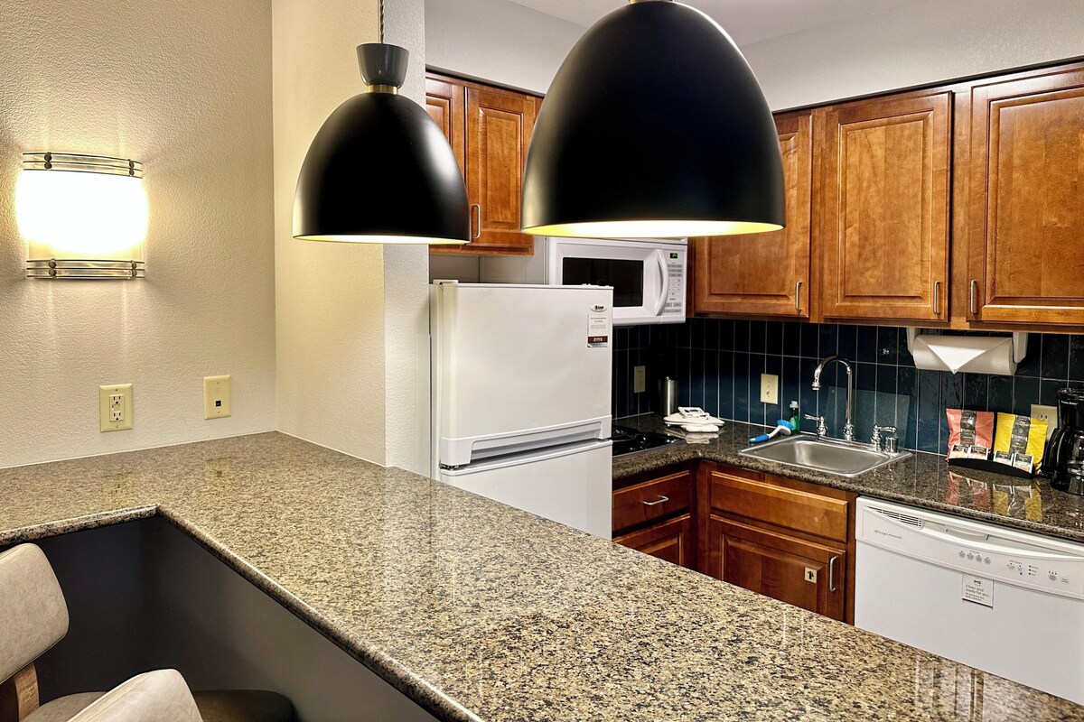 A modern kitchen with granite countertops, wooden cabinets, a white refrigerator, a microwave, and a dishwasher.