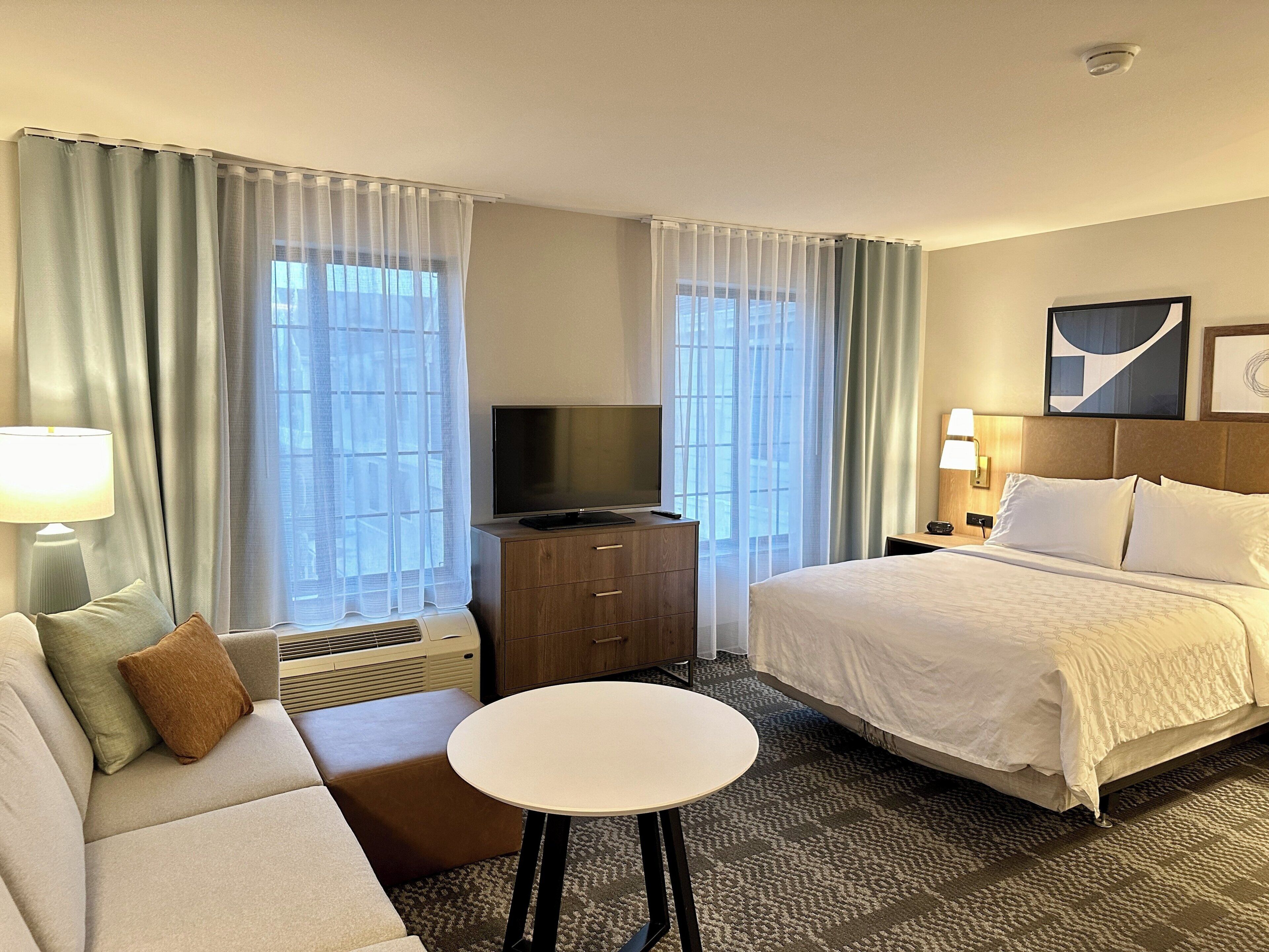 A hotel room with a bed, a sofa, a TV, a small table, and a heater.