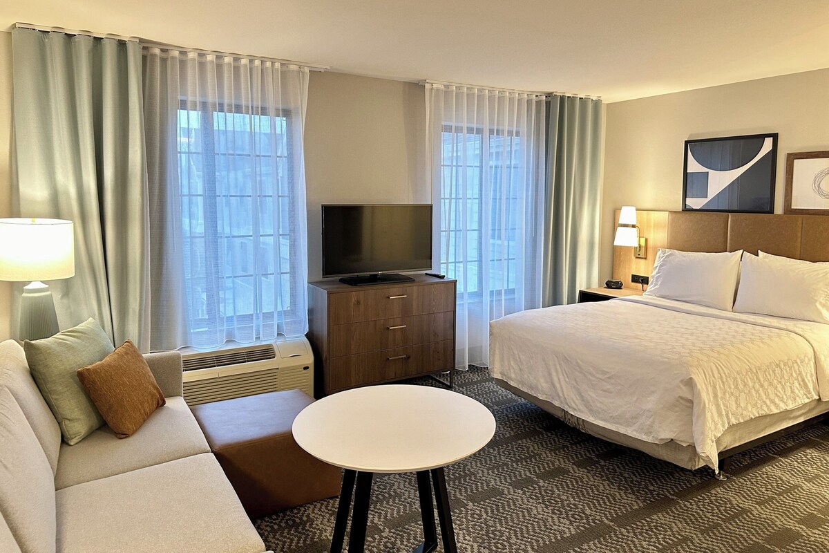 A hotel room with a bed, a sofa, a TV, a small table, and a heater.
