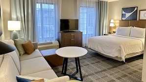 Une chambre d’hôtel avec un lit, un canapé, une télévision, un bureau et une petite table.