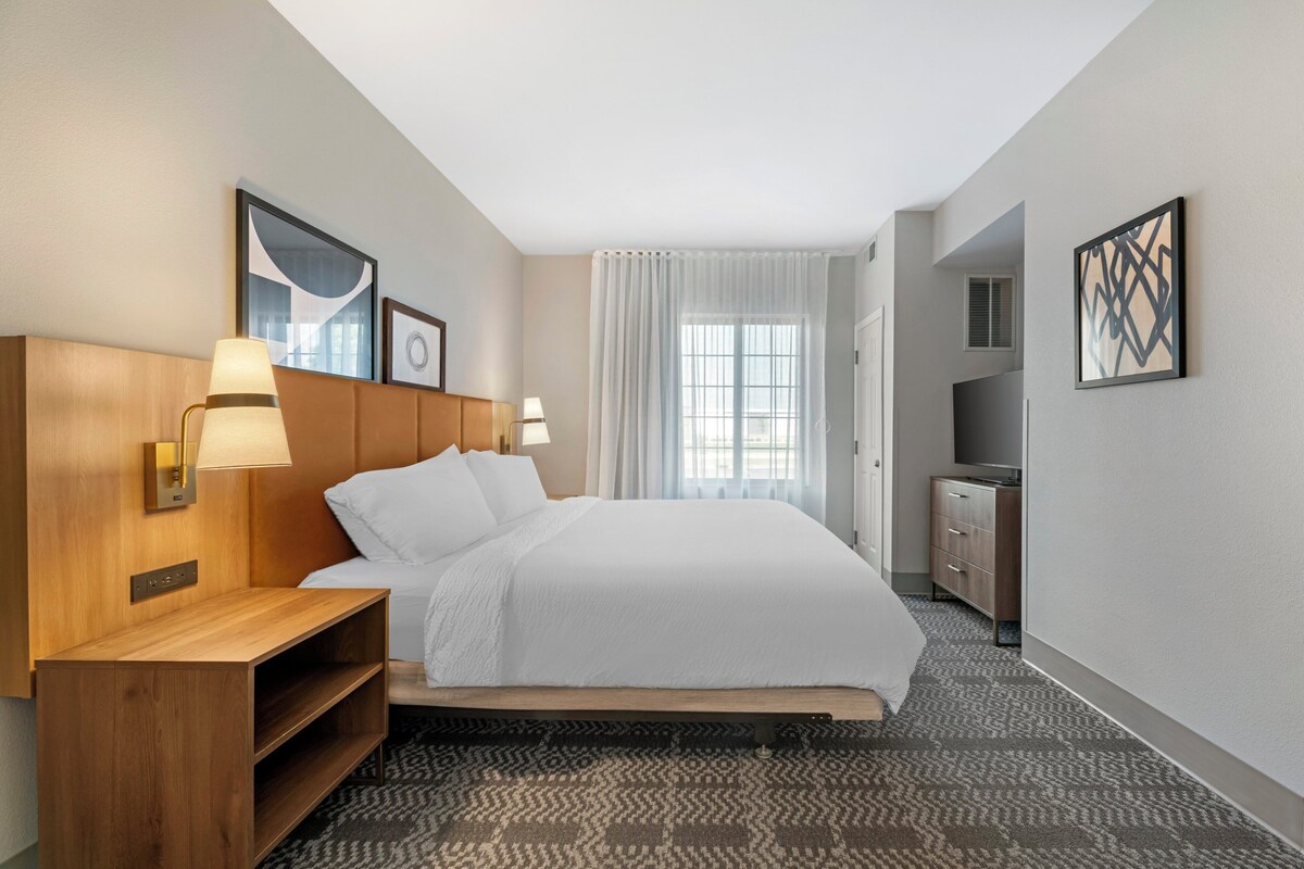 Une chambre d’hôtel avec un lit, des lampes de chevet, une télévision, une armoire et une fenêtre avec des rideaux.