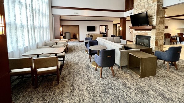 A hotel lobby with a fireplace, seating area, and a TV mounted on the wall. - Staybridge Suites Milwaukee West-Oconomowoc by IHG (Oconomowoc)