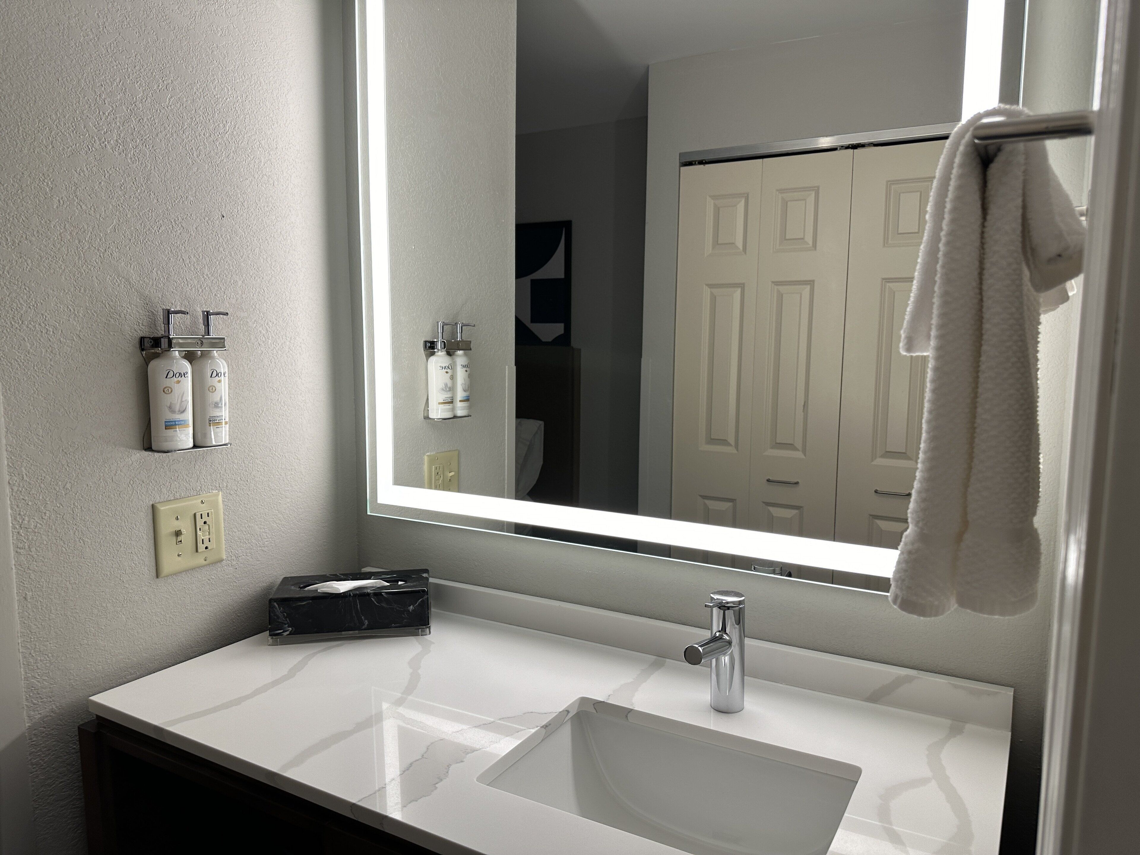 A bathroom with a white sink, a mirror, and toiletries on a shelf.
