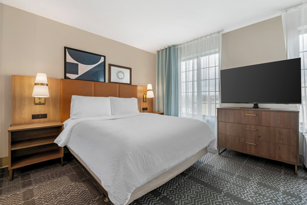 Une chambre d’hôtel avec un grand lit, une télévision, un bureau et une fenêtre avec des rideaux.