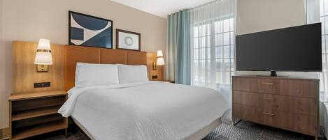 Habitación de hotel con una cama grande, televisión, escritorio y ventana con cortinas.