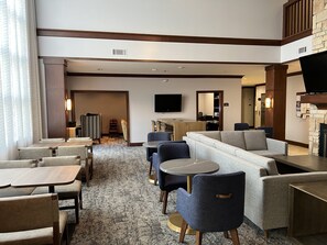 A hotel lobby with a seating area, a flat-screen TV mounted on the wall, and a fireplace. - Staybridge Suites Milwaukee West-Oconomowoc by IHG (Oconomowoc)