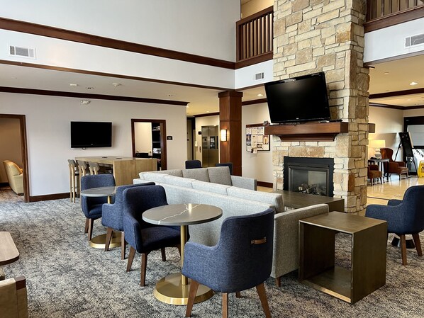 Un vestíbulo de hotel con chimenea de piedra, asientos cómodos, un televisor de pantalla plana y un área de comedor.