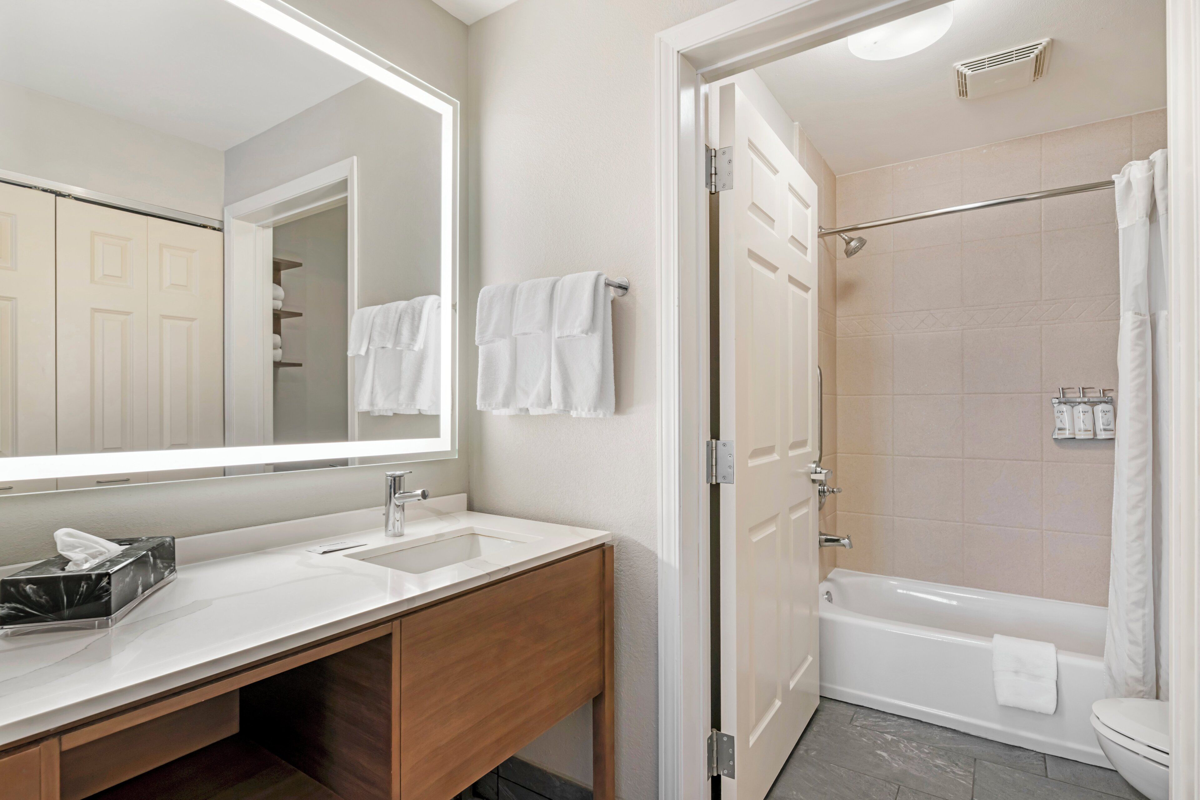 A modern bathroom with a large mirror, a sink, a shower, and a toilet.