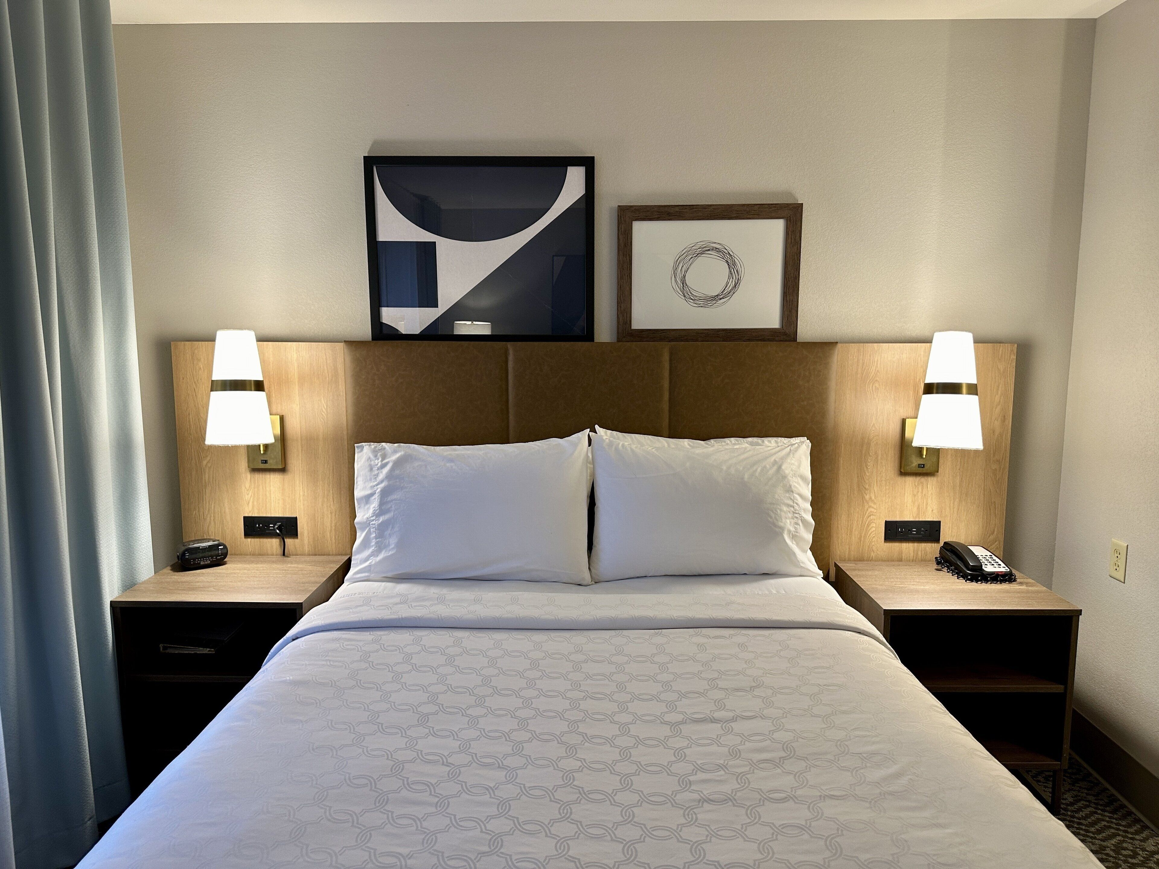 Une chambre d’hôtel avec un grand lit, deux tables de chevet avec des lampes, une œuvre d’art accrochée au mur et un tableau encadré au-dessus du lit.