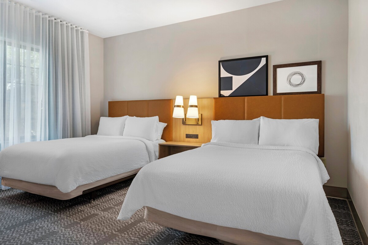 Une chambre d’hôtel avec deux lits, une table de chevet avec des lampes et des œuvres d’art accrochées au mur.