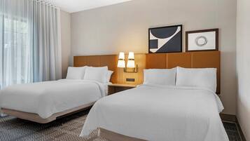 A hotel room with two beds, a nightstand with lamps, and artwork on the wall.
