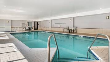 An indoor swimming pool with tiled walls, a door, and a seating area with tables and chairs.