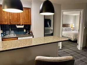 A hotel room with a kitchenette, a bed, and a bathroom.