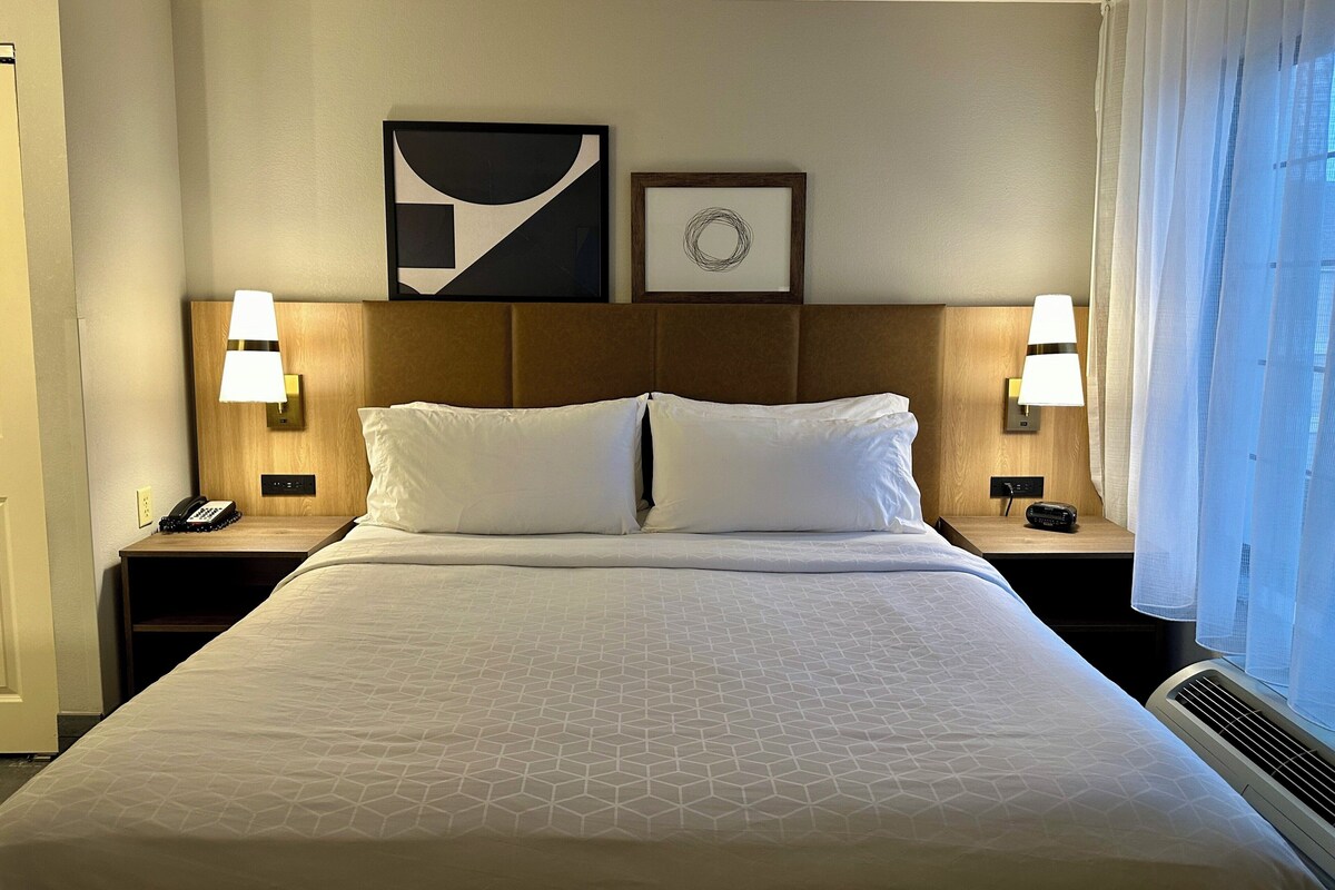 Une chambre d’hôtel avec un grand lit, deux lampes de chevet, un téléphone et un tableau encadré au mur.