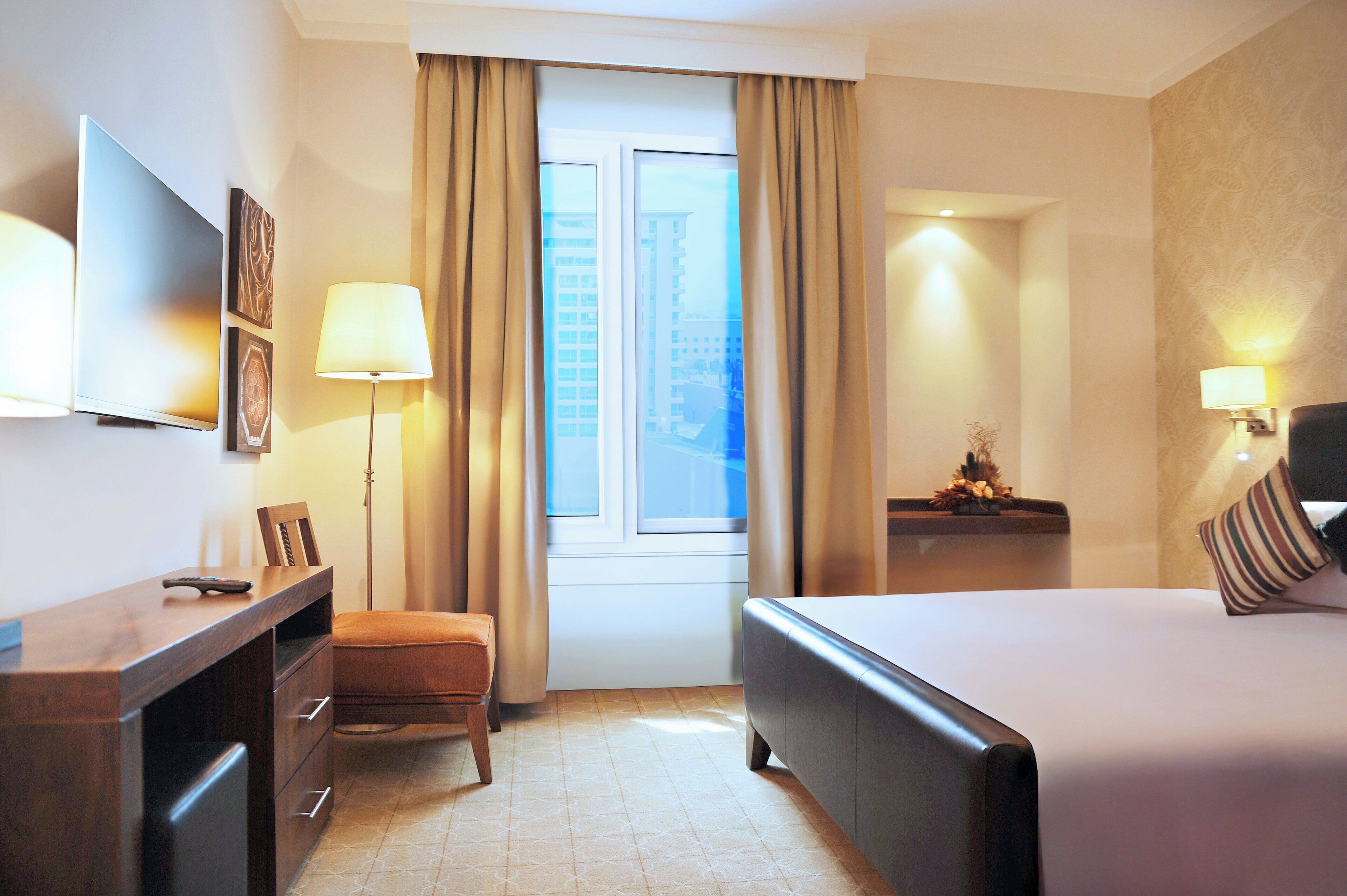 A hotel room with a bed, a desk, a chair, a TV, and a window with curtains.