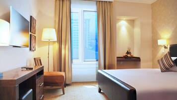 A hotel room with a bed, a desk, a chair, a TV, and a window with curtains.