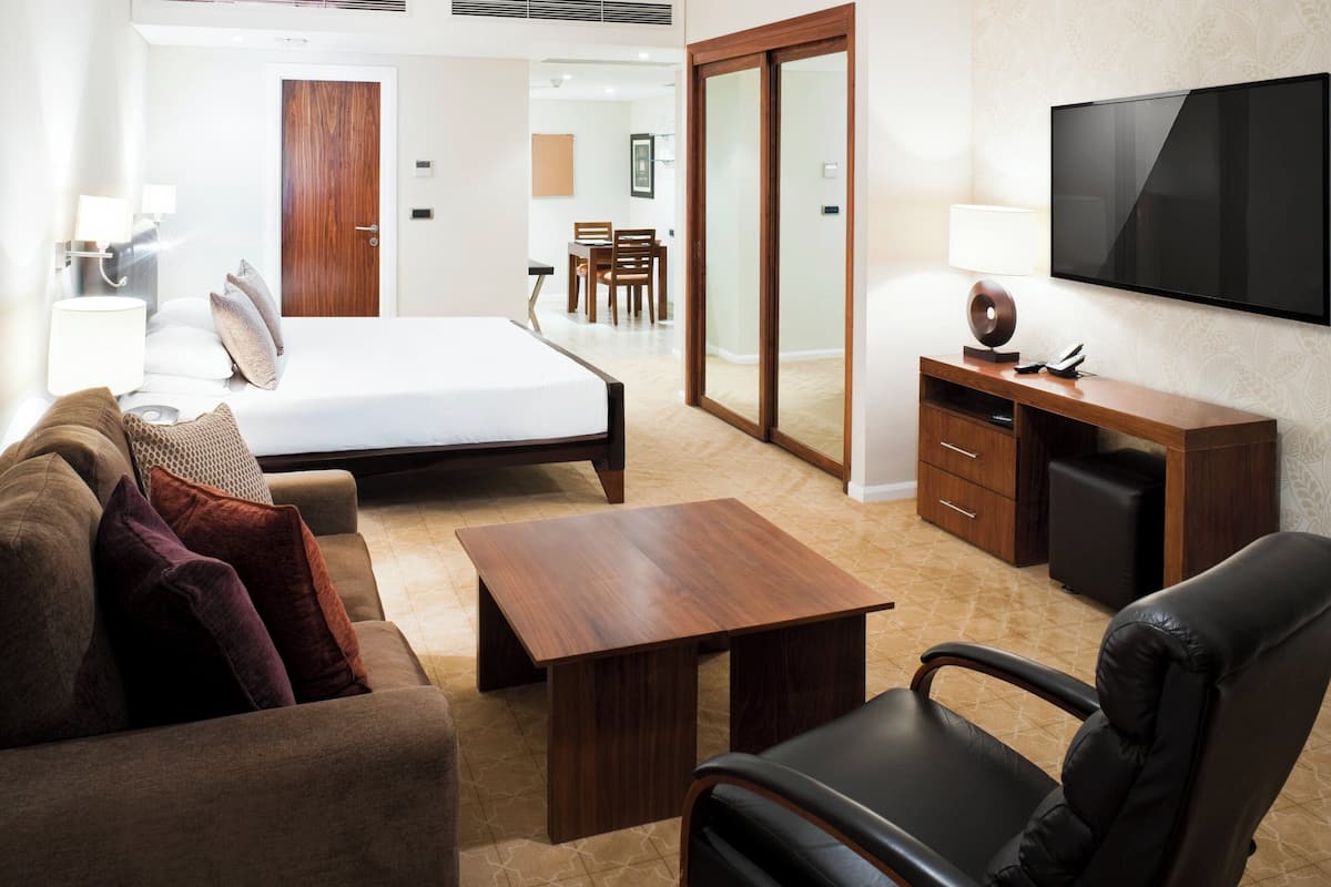 Quarto de hotel moderno com cama, escrivaninha de madeira, televisão, sofá e cadeira.