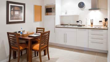 Une cuisine moderne avec des meubles blancs, un four à micro-ondes, une horloge et une table à manger avec des chaises.