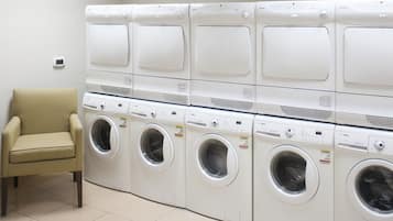 A row of white front-loading washing machines in a laundry room with a beige chair.