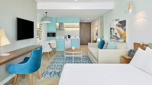 A modern hotel room with a bed, a desk with a lamp, a blue chair, a small round table with a ball, a sofa with cushions, a kitchen area in the background, and a painting on the wall. - Staybridge Suites Cairo Citystars by IHG (Cairo)