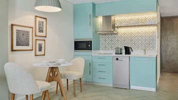 A modern kitchen with teal cabinetry, a microwave, a dishwasher, and a dining area with two chairs and a small table.