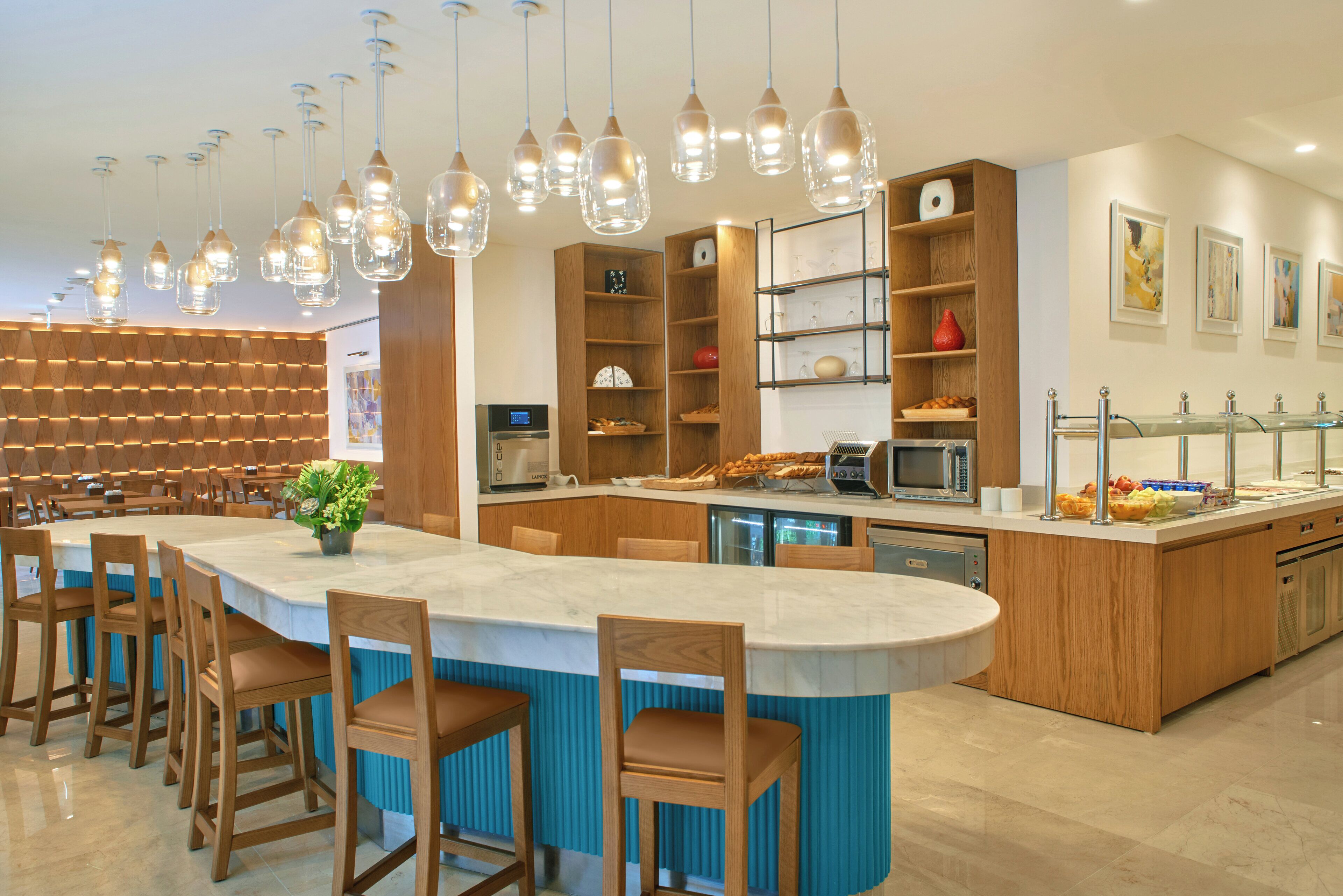 A modern kitchen with a central island, wooden chairs, hanging pendant lights, and built-in shelves.