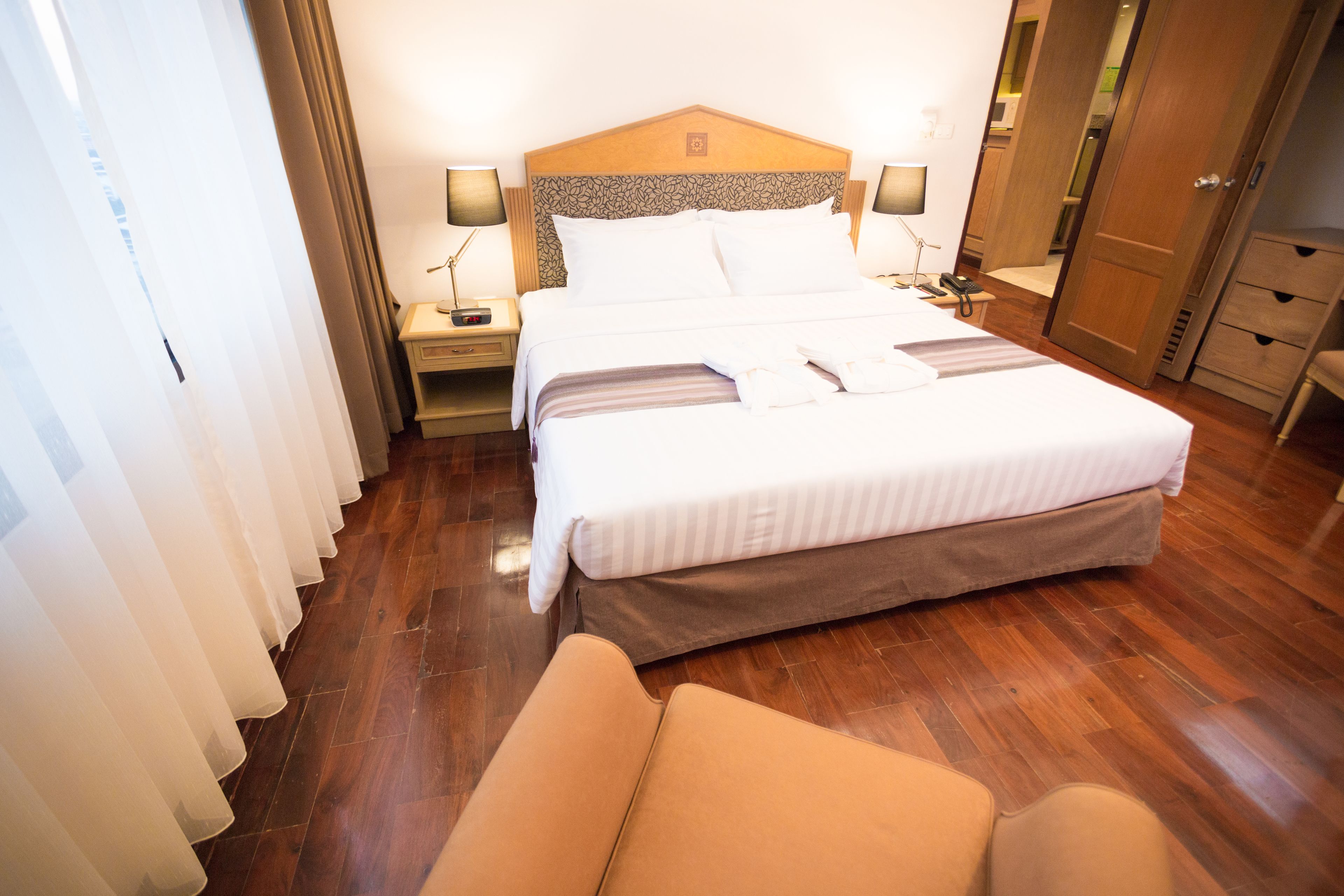 Habitación de hotel con una cama grande, dos mesitas de noche con lámparas, un cabecero de madera y un armario de madera.