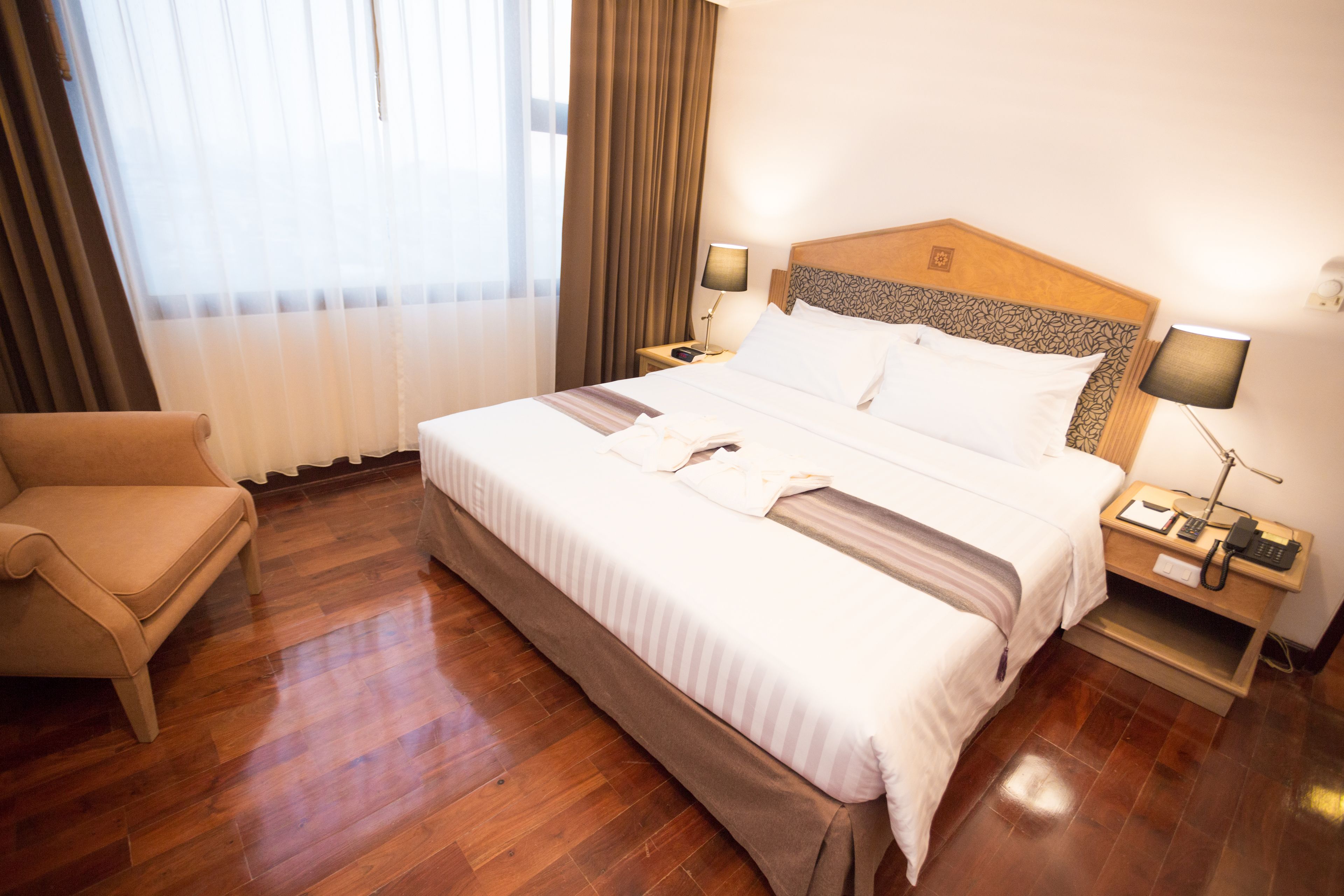 A hotel room with a large bed, two bedside tables, a chair, and a window with curtains.