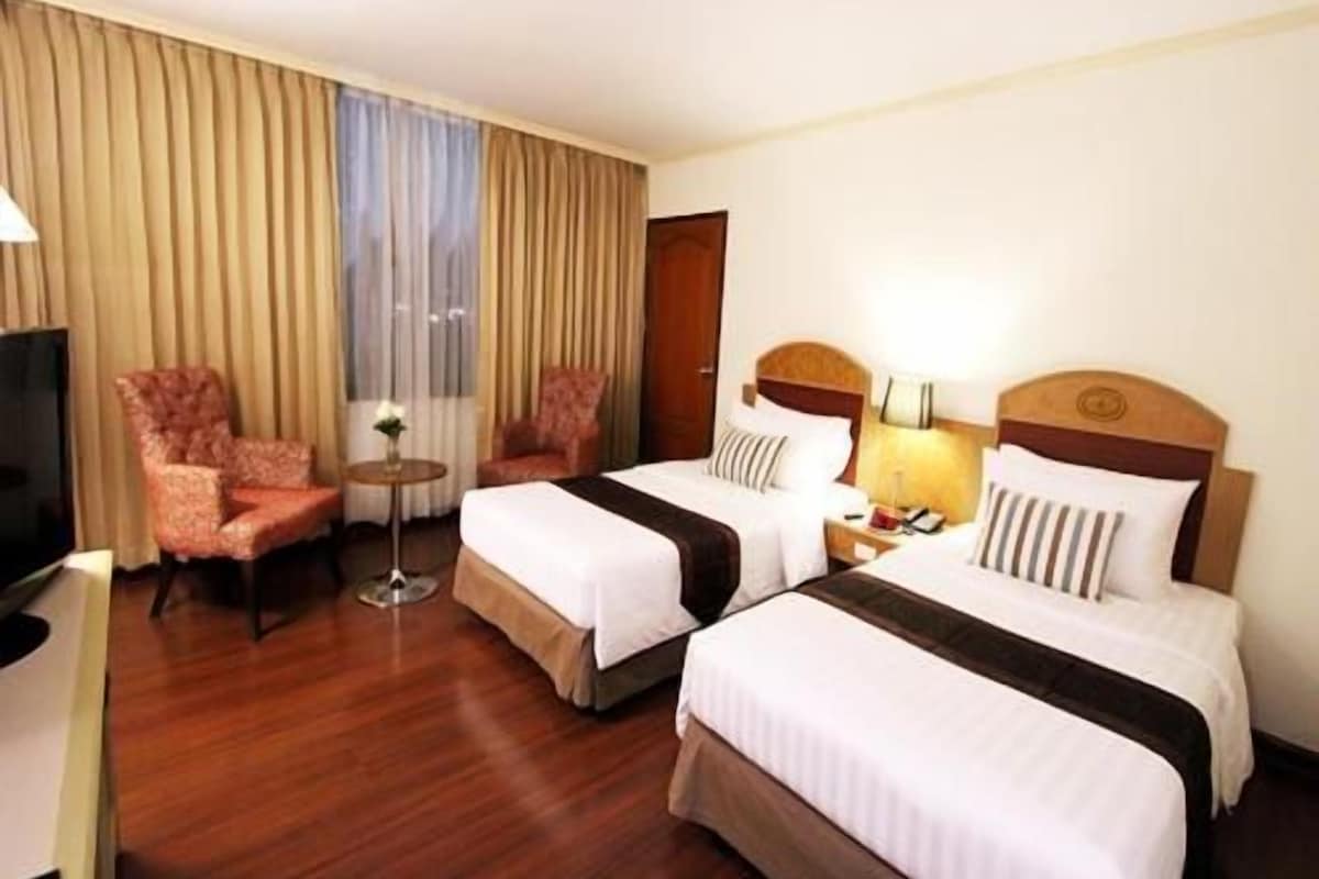 A hotel room with two beds, a TV, a chair, a small table, and curtains.