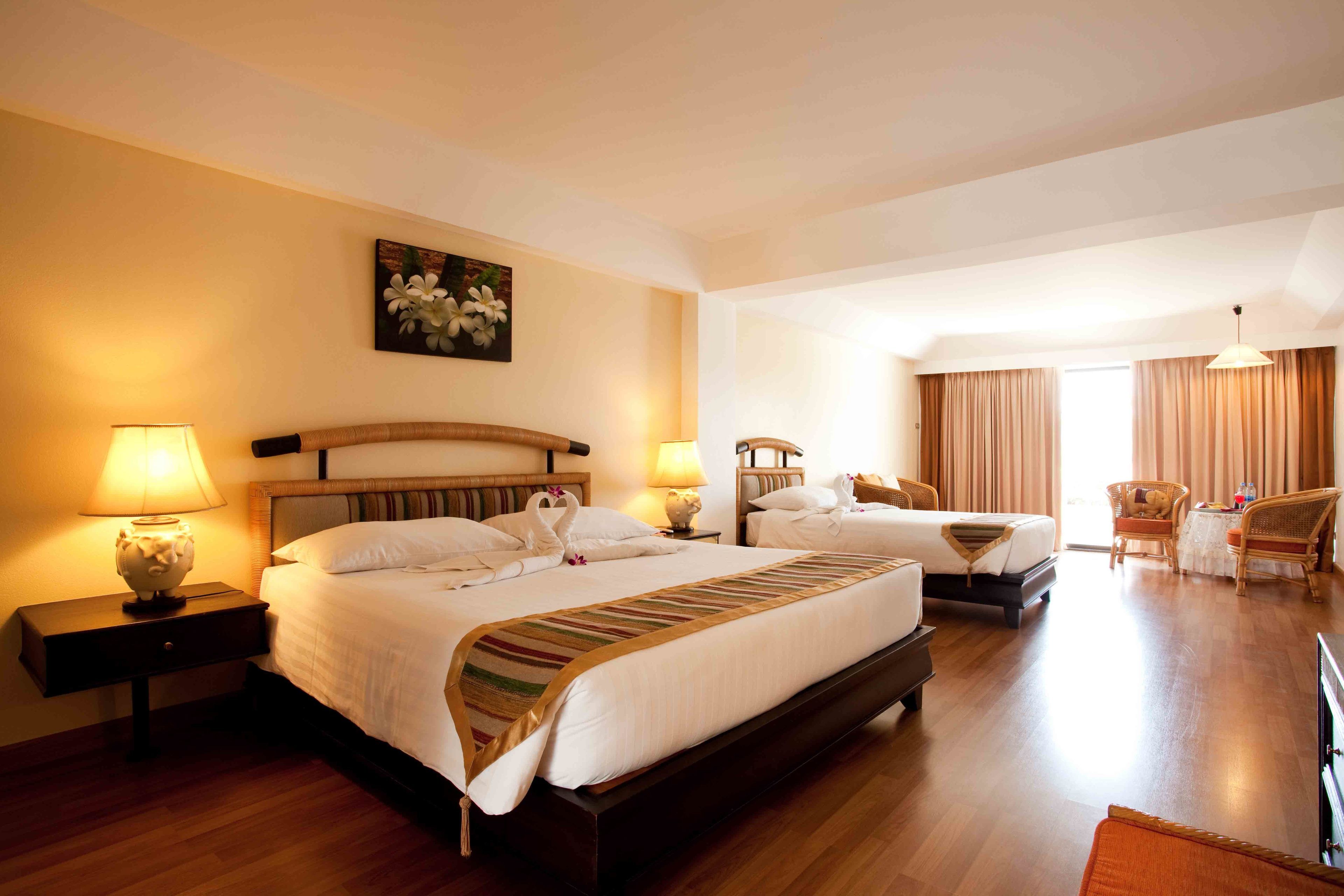 Una habitación de hotel con dos camas, un área de descanso con una silla, una mesa y una lámpara.