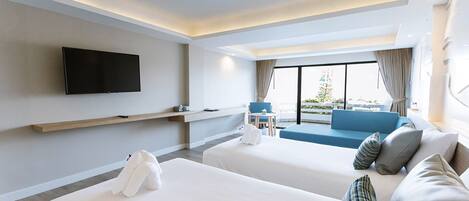 Habitación de hotel con dos camas, un televisor montado en la pared, un sofá y vistas al exterior.