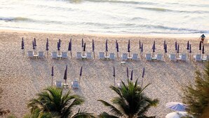 A beach with rows of sun loungers and umbrellas, palm trees, and the ocean in the background. - The Cha-am Methavalai Hotel (Cha-am)